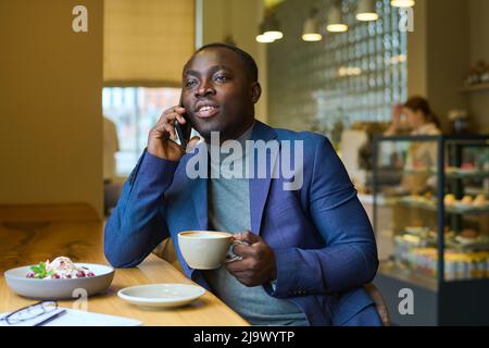 Giovane uomo d'affari africano che ha una conversazione sul telefono cellulare durante la pausa caffè al bar Foto Stock