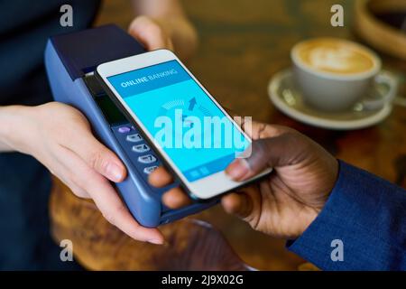 Primo piano di un uomo che mette il suo smartphone al terminale e paga online per il suo ordine in caffetteria Foto Stock