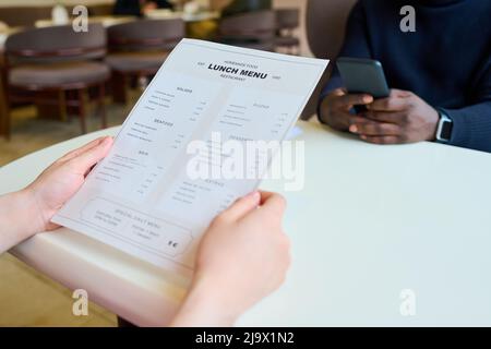 Primo piano di una donna irriconoscibile che legge il menu mentre si siede al tavolo con la sua collega durante il pranzo d'affari in caffetteria Foto Stock