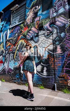 Ragazza che cammina attraverso una strada posteriore graffitata a Brighton Foto Stock