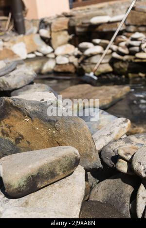 Grandi pietre sporche sullo sfondo della piscina. Costruzione e pulizia di un laghetto ornamentale nel giardino. Disegno paesaggistico. Foto Stock