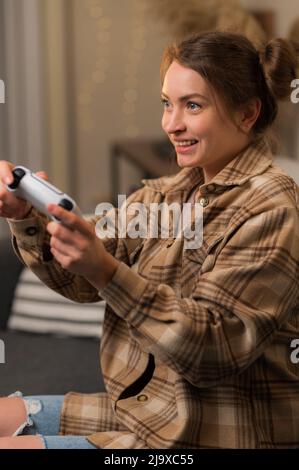 Primo piano. Ragazza gamer in una camicia a quadri con un gamepad nelle sue mani emotivamente gioca video giochi con gli amici. Tempo libero, hobby, relax, divertimento passatempo. Foto Stock