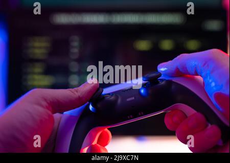 Un giocatore con un joystick nelle sue mani gioca a videogiochi con gli amici online. Background tecnologico. Cultura giovanile, hobby, strategia di gioco, rea virtuale Foto Stock