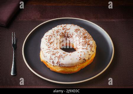 Gustosa ciambella isolata su un piatto su un tavolo fine. Ciambelle, con cioccolato bianco cosparso di gocce di cioccolato, dolci raffinati Foto Stock