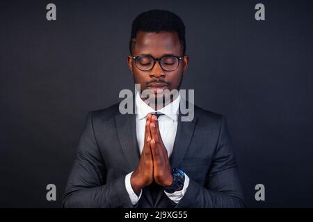 Grazie a Dio per tutto ciò che ho. afro american business ADVISOR uomo che prega e meditando, mano segno calma gesto dal fronte nero sfondo in Foto Stock