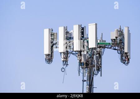 Primo piano della torre del telefono cellulare per telecomunicazioni con antenne di comunicazione wireless; sfondo blu e spazio di copia sulla destra Foto Stock