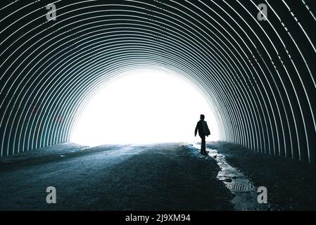 I bambini camminano da soli accanto al torrente che passa attraverso il tunnel di metallo scuro. Foto Stock