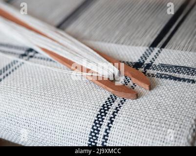 Progetto di tessitura in bianco e nero. Navetta in legno con filo sul telaio, primo piano Foto Stock