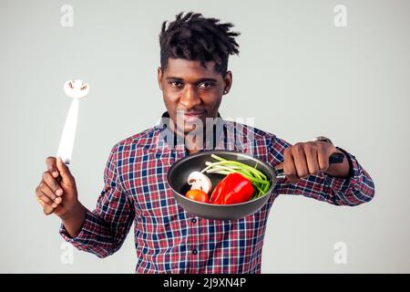 chef afroamericano kitchener che tiene una padella wizard man cucina magica flying food insalata, carota, aglio, cipolla, pepe, patate, cetrioli Foto Stock