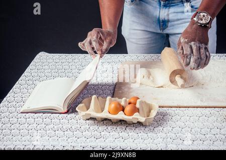 African American cuoco maschile chef vanta di mani di pasticceria in farina di cottura .man`s fogli di pasta con rolling pin torta, le uova e ricetta Foto Stock