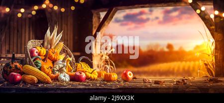 Cestino di Pumpkins, mele e mais su Harvest Table in Barn con porta aperta e sfondo tramonto - Harvest e Thanksgiving Foto Stock