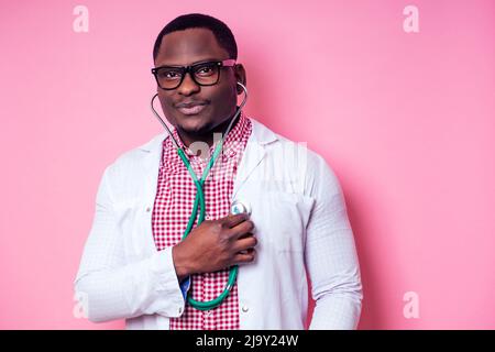 felice medico chirurgo medico africano medico medico medico medico medico medico medico in un cappotto bianco su uno sfondo rosa in studio. Foto Stock