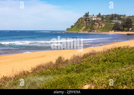 Newport Beach una delle spiagge settentrionali di Sydney, persone che camminano sulla sabbia, case sulla scogliera sul promontorio di Bungan, Sydney, NSW, Australia in autunno Foto Stock