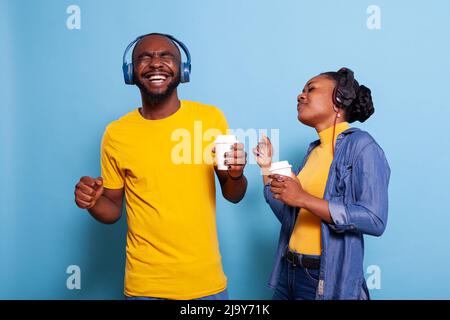 Una coppia felice balla e ascolta la musica con le cuffie, facendo divertenti mosse di danza sulla fotocamera. Uomo e donna romantici che si divertono con mp3 canzoni in cuffia. Persone con audio che ride. Foto Stock