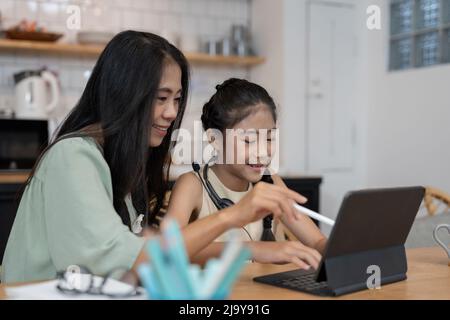 Giovane madre asiatica con computer notebook che insegnano al bambino per imparare o studiare in linea a casa, concetto in linea di Homeschooling Foto Stock