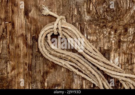 Bobina di vecchia corda su sfondo di legno scuro. Fune sporca e usurata. Superficie di legno incrinata con crepe e trucioli. Messa a fuoco selettiva. Foto Stock