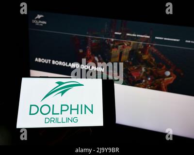 Persona che tiene il cellulare con il logo della società Dolphin Drilling Holdings Limited sullo schermo di fronte al sito web aziendale. Mettere a fuoco sul display del telefono. Foto Stock
