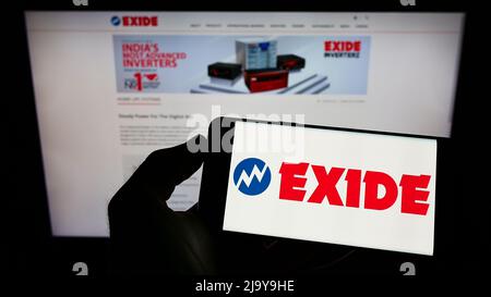 Persona che tiene il cellulare con il logo della società indiana di batterie Exide Industries Ltd. Sullo schermo di fronte al sito web aziendale. Mettere a fuoco sul display del telefono. Foto Stock