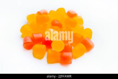 Primo piano di grumi multivitaminici arancioni e gialli sotto forma di orsi su sfondo bianco. Foto Stock