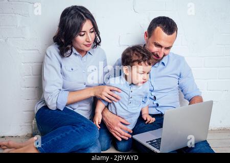 famiglia felice bella madre piccolo figlio e padre giocare a sviluppare gioco per bambini online in un portatile in appartamento seduto sul pavimento Foto Stock