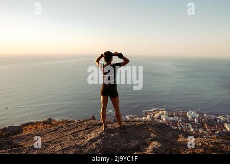 Vista posteriore del runner in piedi sul bordo e godere della vista al tramonto Foto Stock