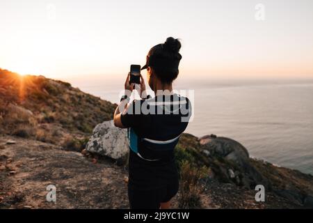 Vista posteriore donna escursionista fare foto del tramonto sul suo smartphone Foto Stock