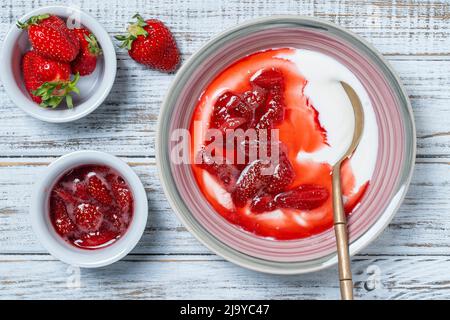 Piatto bianco con fragole rosse e yogurt naturale su un tavolo in legno, da vicino, vista dall'alto Foto Stock
