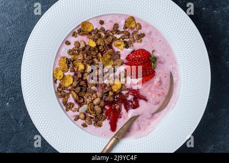 Piatto bianco con fragole rosse, granola e yogurt naturale su sfondo nero, da vicino, vista dall'alto Foto Stock