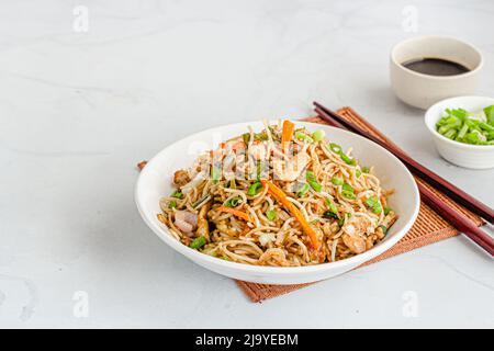 Una ciotola di Chicken Chow Mein con salsa di cipolla e soia su sfondo bianco Foto Stock