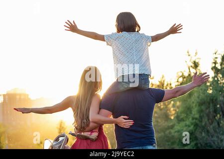 Felice fotosessione attiva di famiglia nel parco estivo. Bella donna dai capelli lunghi il suo uomo con sua figlia e figlio in un passeggino riposo sulla natura Foto Stock