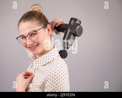 Donna sorridente con bretelle usa una pistola massaggiatore per la schiena. Foto Stock