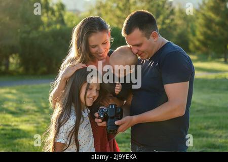 la famiglia felice sta riposando nel parco in estate. bella madre, bel padre con un bambino piccolo ragazzo e figlia carina fotografata con la macchina fotografica Foto Stock