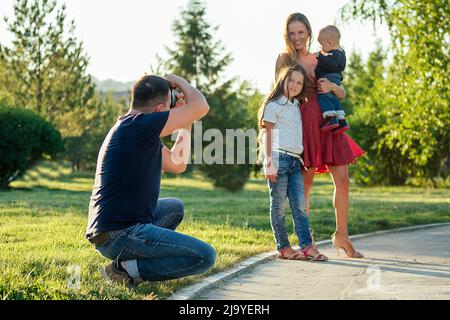 la famiglia felice sta riposando nel parco in estate. bella madre, bel padre con un bambino piccolo ragazzo e figlia carina fotografata con la macchina fotografica Foto Stock