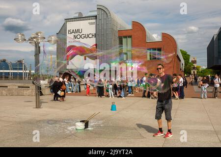 Colonia, Germania - 17 maggio 2022 : Un artista di strada che fa gigantesche bolle di sapone di fronte a una folla giovane di persone Foto Stock