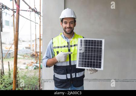 Giovane ingegnere in giacca di sicurezza hardhat e guanto puntando dito verso il pannello di celle solari, presentare una fonte di energia per generare corrente continua di elettricità Foto Stock