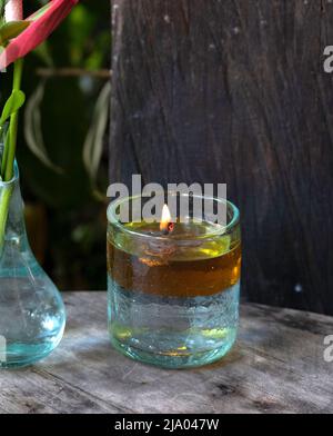 Fiamma fluttuante che brucia in un contenitore spesso a forma di vetro d'acqua su tavola di legno accanto al vaso di vetro con un'occhiata a fiore esotico Foto Stock