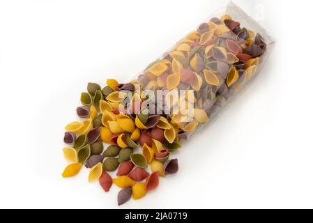 Conchiglie di pasta colorata che fuoriescono da sacchetto trasparente, semola di grano duro con curcuma, spinaci, barbabietole e carro nero Foto Stock