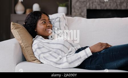 Happy rilassato african american donna riposo lounge sdraiato sul divano godere tranquillo mood week-end casual riposo in soggiorno sul divano pigro calma ragazza sognare Foto Stock