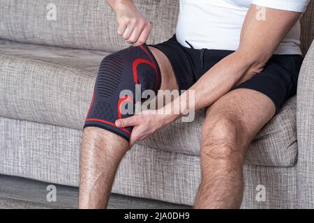 Il ragazzo mette un bendaggio a compressione sul ginocchio ferito. Preparandosi per le attività sportive, il punto dolente è evidenziato in rosso Foto Stock