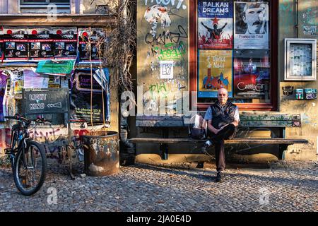 Uomo anziano seduto su panchina fuori dal vecchio cinema storico di Lichtblick a Kastanienalle, Prenzlauerberg, Berlino Foto Stock