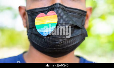 primo piano colpo di uomo con orgoglio o simbolo di cuore arcobaleno sulla maschera medica del viso durante coronavirus covid-19 pandemic pride march - concetto di solidarietà Foto Stock