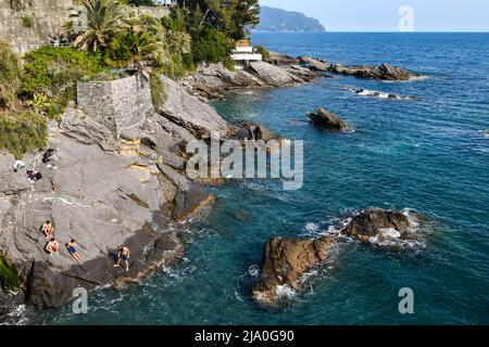 Vista rialzata della costa rocciosa della Promenade Anita Garibaldi con i ragazzi che prendono il sole e il promontorio di Portofino sullo sfondo, Nervi, Genova Foto Stock