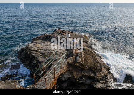 Vista rialzata di persone che siedono su una roccia dal mare collegato alla scogliera della passeggiata di Nervi con un passaggio in pietra, Genova, Liguria, Italia Foto Stock