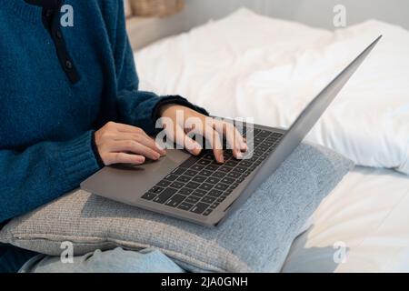 Primo piano sulle mani di una specialista femminile che lavora su un computer portatile in un accogliente salotto di casa mentre si siede a un tavolo. Donna freelance che chiacchiera Foto Stock