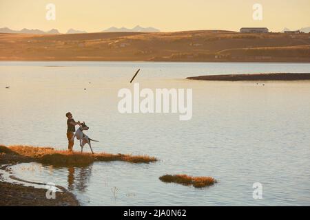 Un ragazzo gioca con il suo cane sul lago Argentino al tramonto, El Calafate, Patagonia, Argentina. Foto Stock