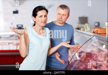 Triste coppia di clienti adulti che scelgono la carne in negozio Foto Stock