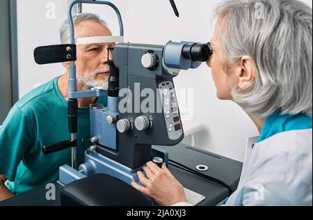 Optometristo esperto che fa il test della vista per l'uomo anziano alla clinica moderna di oftalmologia. Esame visivo e diagnostica visiva Foto Stock