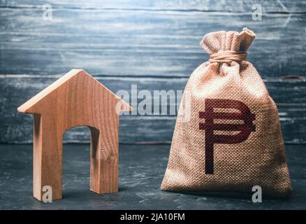 Casa di legno e un sacchetto di soldi del peso filippino. Mutuo ipotecario. Sviluppo di progetti di casa. Attività di noleggio. Servizi di realtor. Generare reddito da affitto Foto Stock