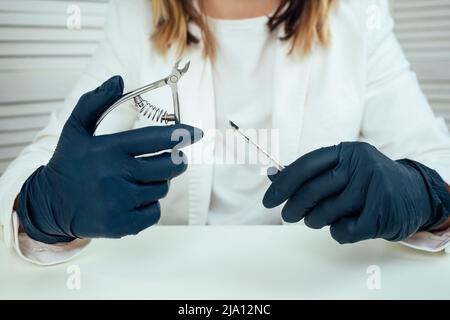 primo piano mani di manicurista professionista maestro di manicure donna in una giacca bianca e in guanti di gomma nera tenere cuticola strumento di rimozione in una bellezza Foto Stock