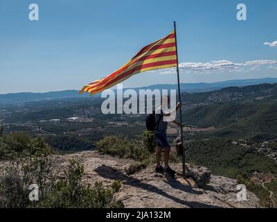 Un escursionista che tiene e sventola la bandiera della Catalogna sulla cima della montagna Foto Stock